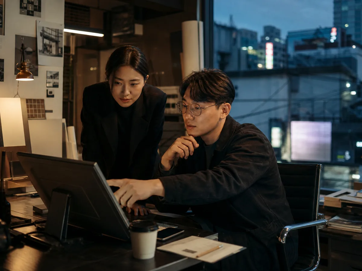 Two Korean business owners reviewing a screen in a small studio, bright light