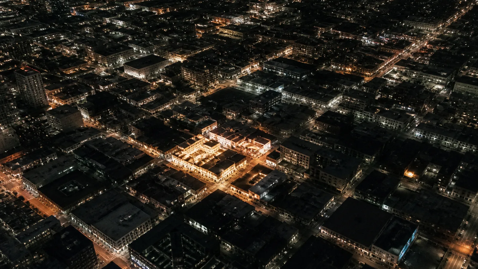 Overhead night view of a dense city grid with warm street lights, a few blocks glowing brighter, suggesting local search