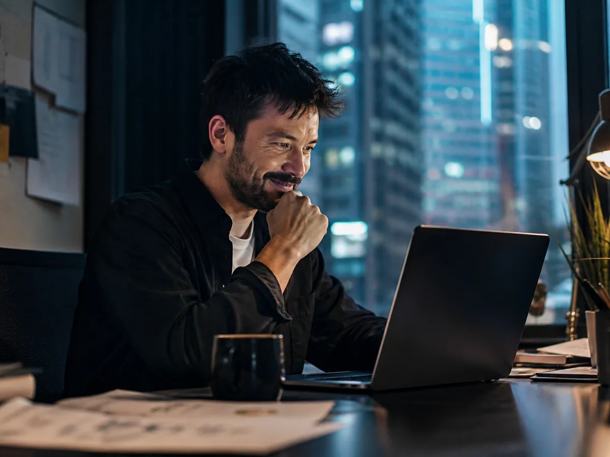 Business owner reading reviews on a laptop and smiling, small office, window light